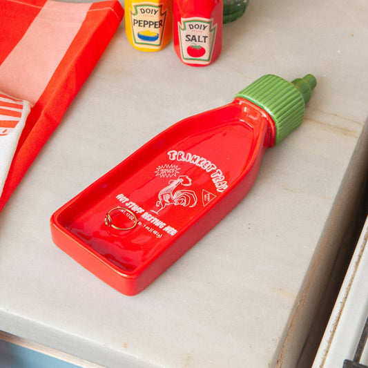 Red sriracha bottle-shaped container on a kitchen counter with condiment bottles in the background.