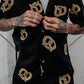 Person with heavily tattooed arms buttoning up a black shirt with all-over pretzels print.