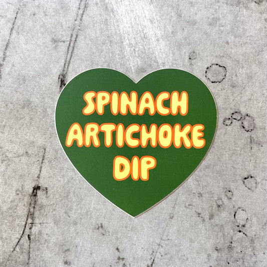 Green, heart-shaped sticker with "Spinach Artichoke Dip" printed in light yellow bubble letter font..