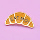 Enamel pin in the shape of a croissant that says "EAT MOI"