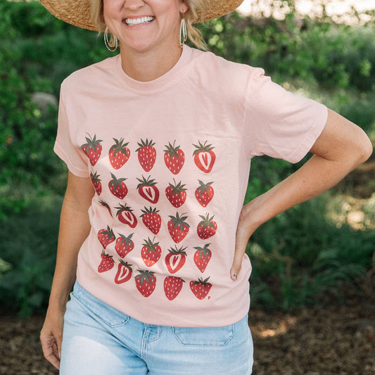 Farmer wearing peachy pink tee with repeat print of whole and halved strawberries.