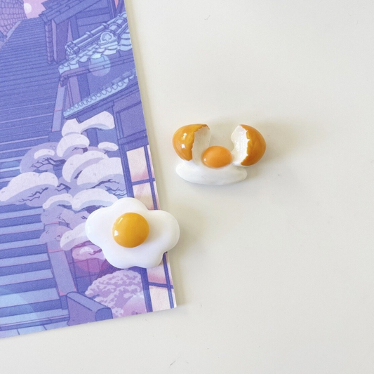Set of two magnets, one fried egg and one raw egg freshly cracked with shells on side.