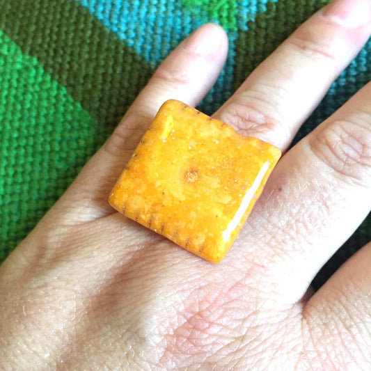Cheez-it covered in resin to make a ring. Shown here on a person's left ring finger. 