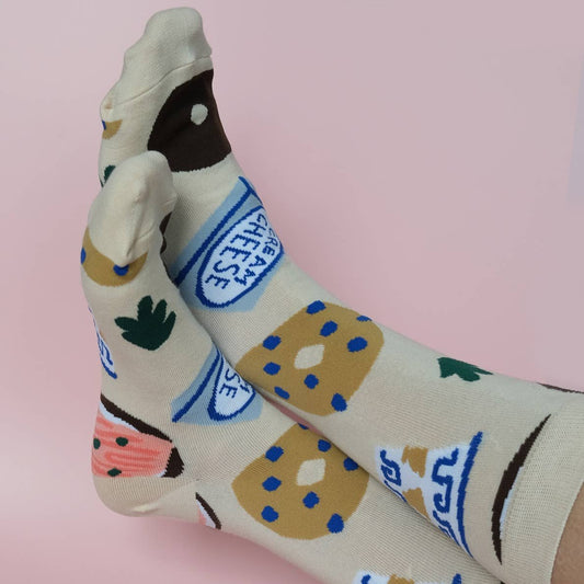 Bagel socks on models feet -- design features bagels, coffee cup, cream cheese and lox