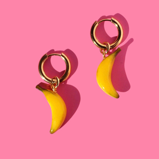 Gold hoop earrings with banana-shaped charms on a pink background