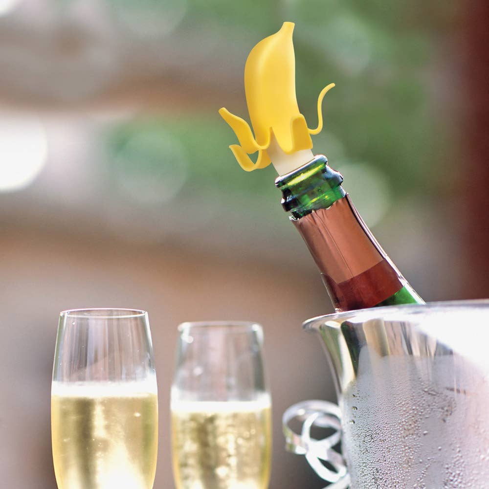 Banana-shaped bottle stopper on a wine bottle with two glasses of champagne and an ice bucket in the background.