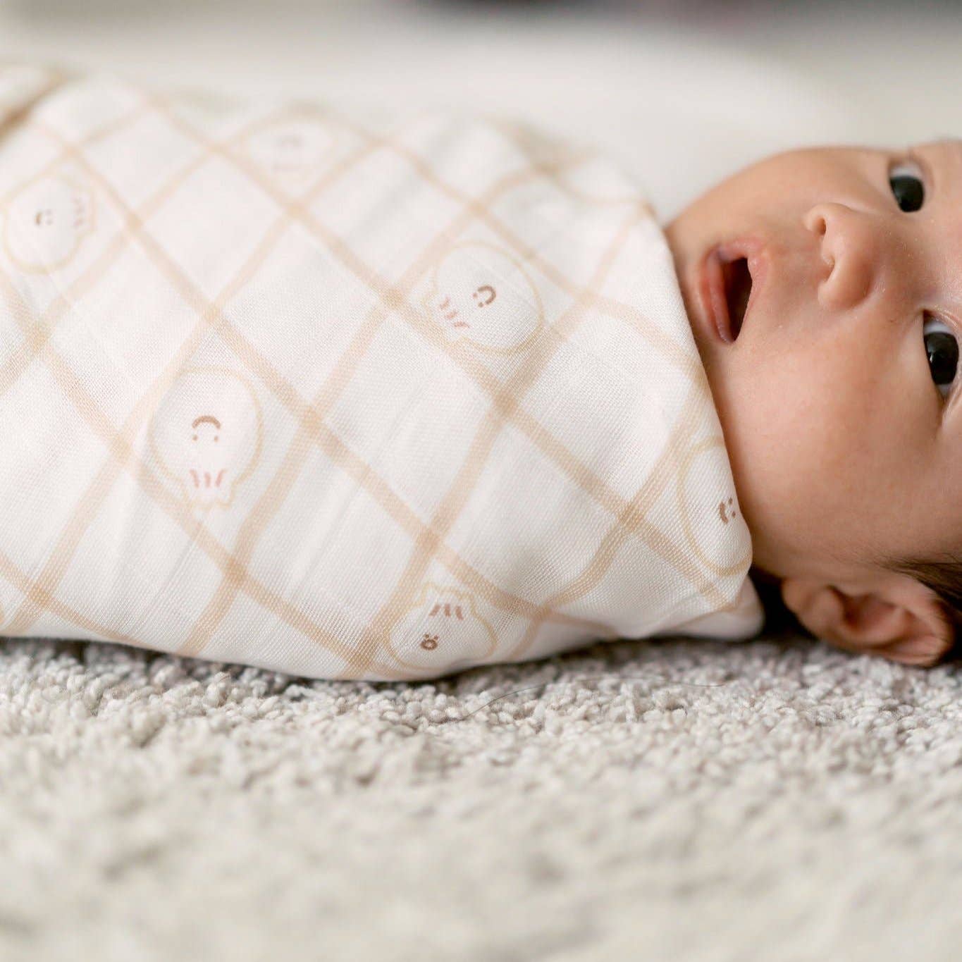 Baby wrapped in a patterned swaddle on a soft surface