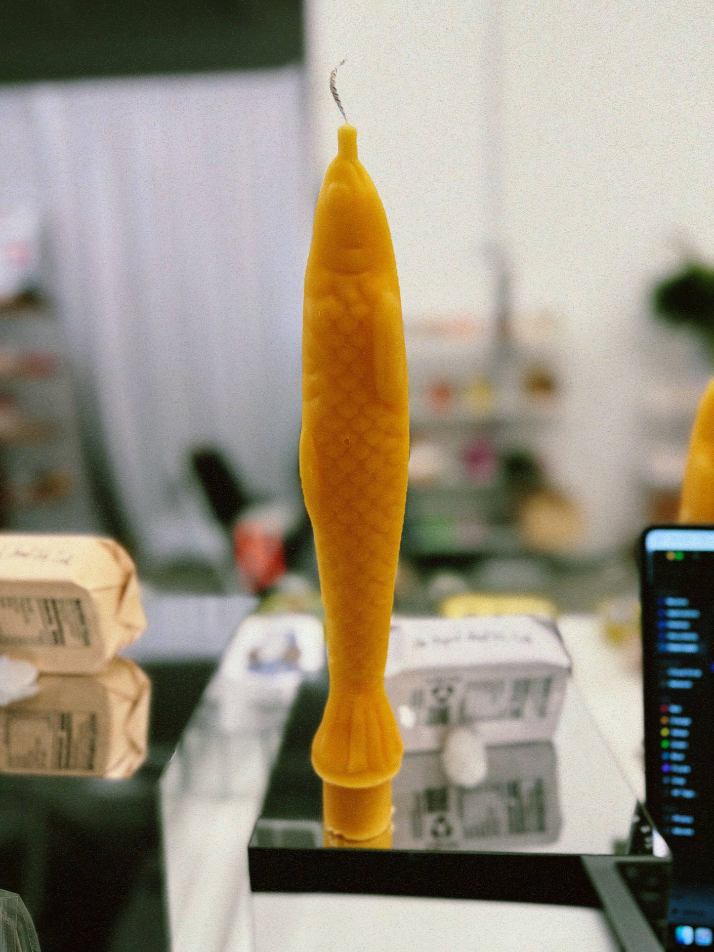 Single yellow beeswax taper candle shaped like a fish. Shown unwrapped on countertop.
