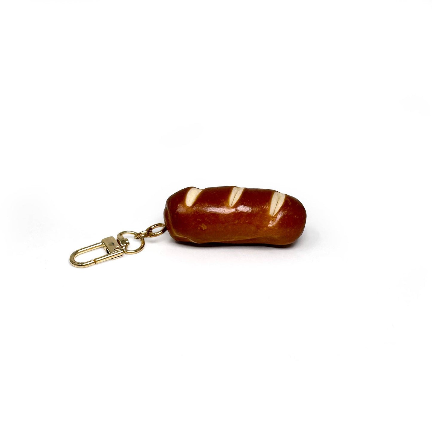 Keychain shaped like a realistic baguette (or pretzel roll) with toasty brown crust scored diagonally three times.