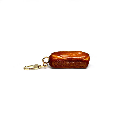 Keychain shaped like a realistic baguette (or pretzel roll) with toasty brown crust scored diagonally three times.