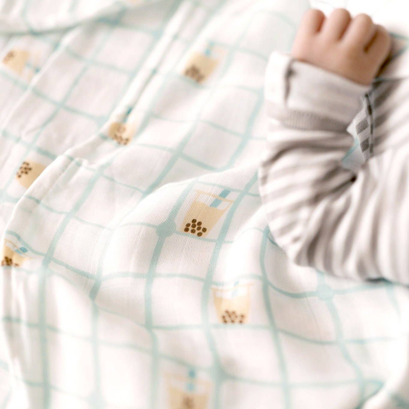 Close-up of a baby's hand reaching through a textured blanket with paw print patterns.