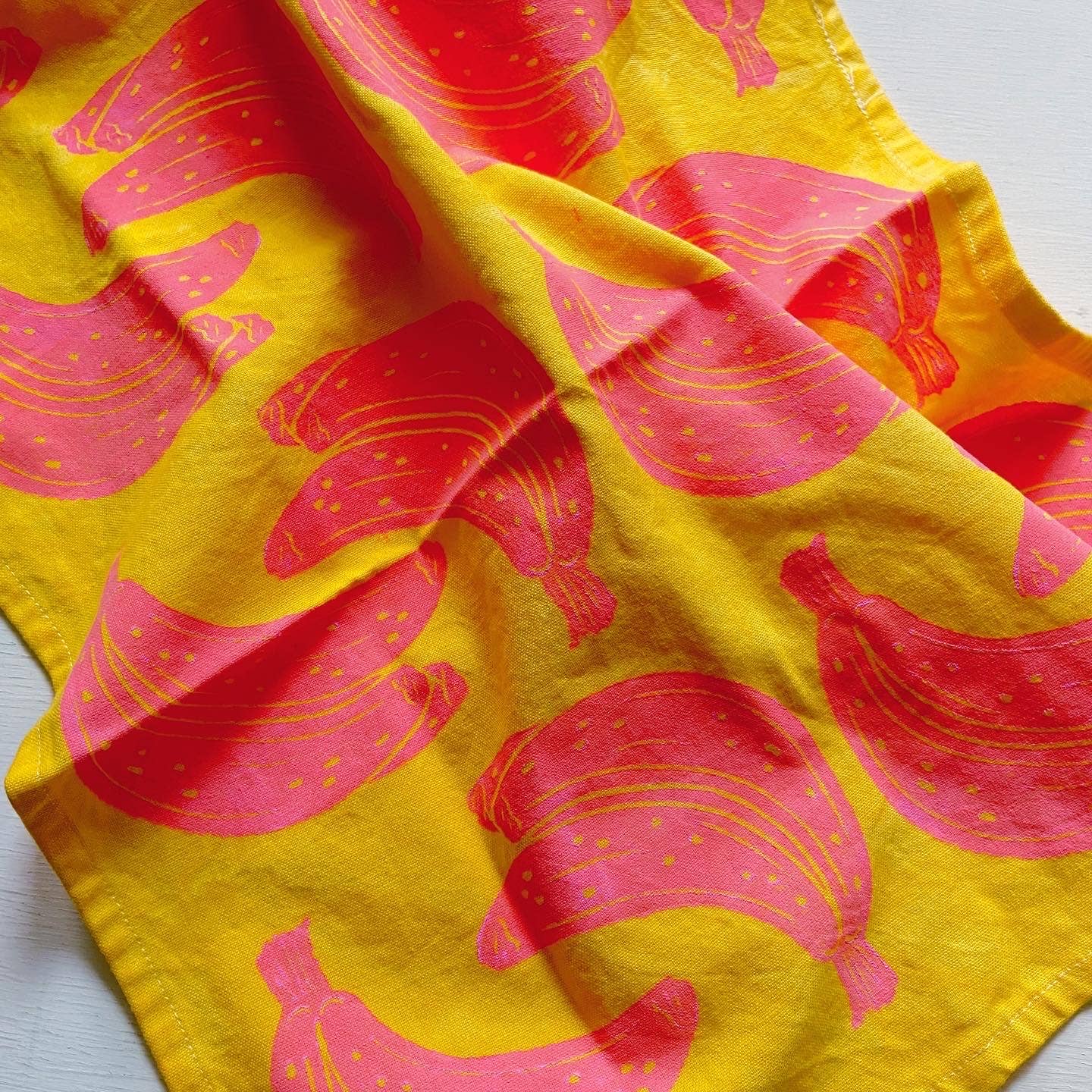Bright yellow kitchen towel with pink bananas printed on as the design pattern