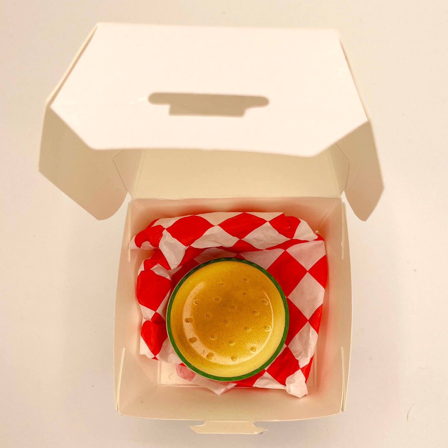 Butane lighter shaped like a hamburger. Shown on top of red and white checkered deli paper inside takeaway box.