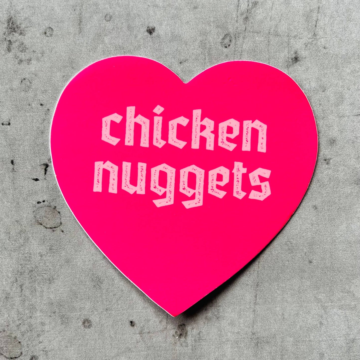 pink, heart shaped sticker with text that reads "chicken nuggets" on it