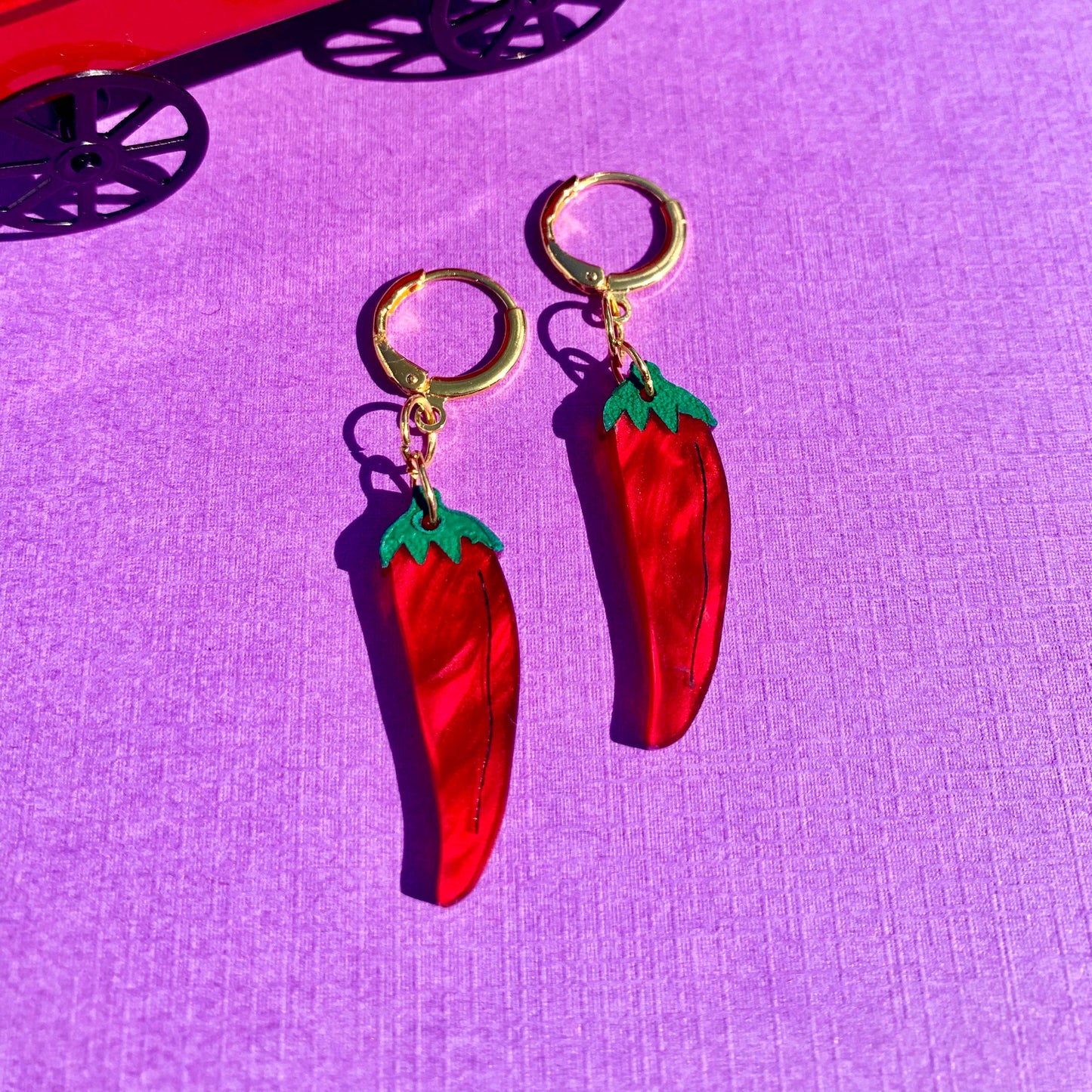 Red chili pepper earrings on a purple surface with a red toy truck in the background.