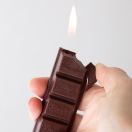 Refillable lighter shaped like a chocolate bar with four sections and "Chocolate" in script font imprinted on each section. Shown in the process of being lit by pressing a small chunk or "bite" on the side.