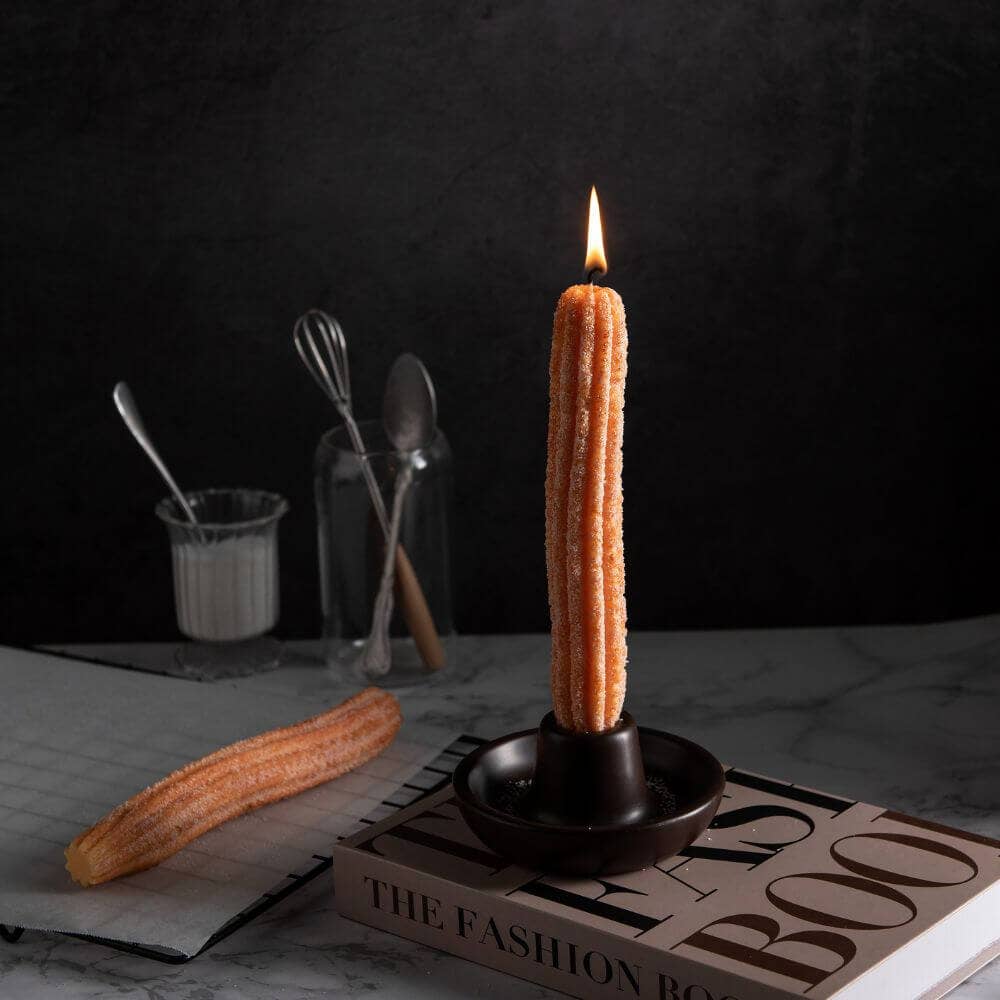 Churro tapered candles set in a backdrop with kitchen utensils. The candle is lit.