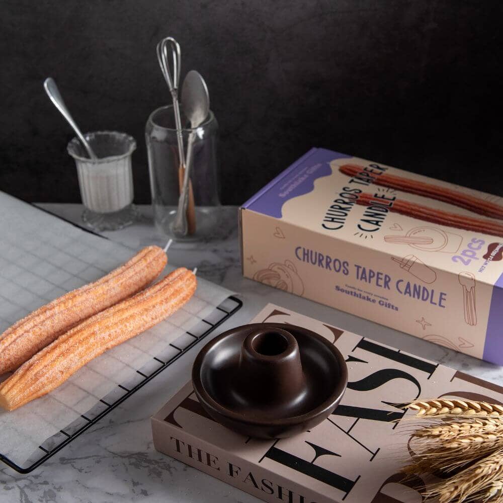 Display of the Churro Candles on a baking rack with parchment paper. The display box is show as is the candle holder that the Churro Candles come with.