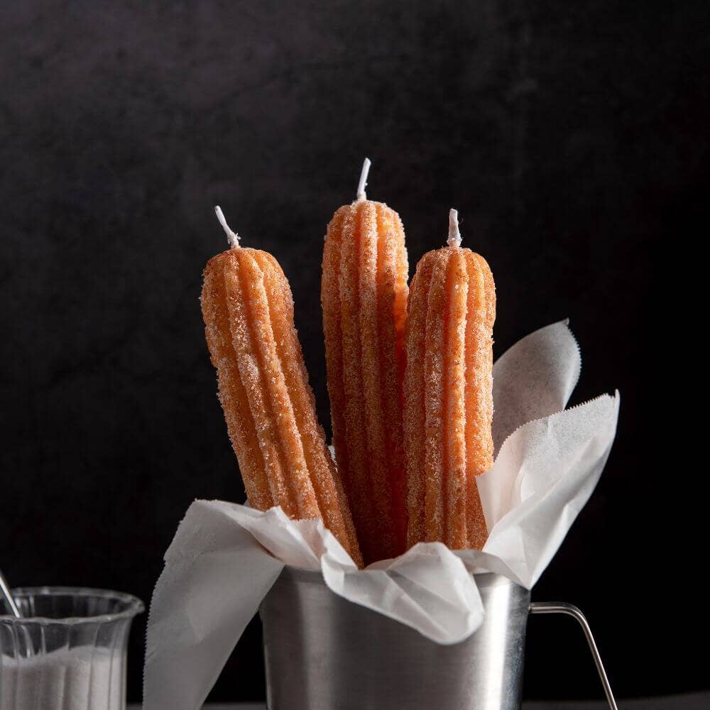 Three Churro Candles in a display cup with a side of granulated sugar.
