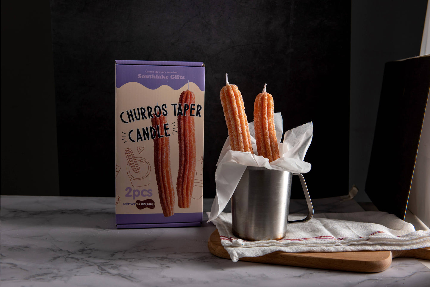 Churro Tapered Candles in a display cup with the retail box behind it. The box says: Southlake Gifts; Churro Taper Candle; 2pcs