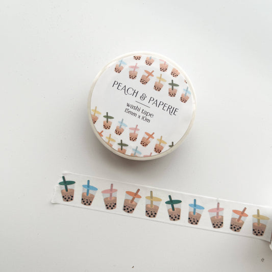 A roll of Peach & Paperie washi tape with a white label and a strip of the tape unrolled below, featuring a repeating pattern of boba tea cups in pastel colors on a white background.