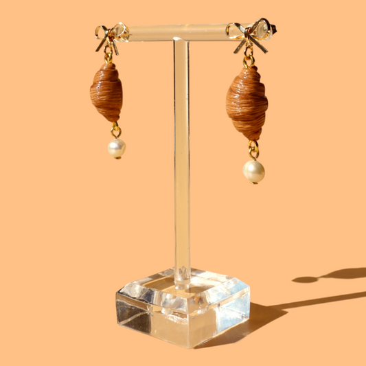 Pair of earrings with croissant beads and pearls on a clear stand against an orange background