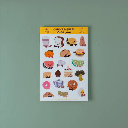 Sticker sheet with 20 cute food-themed stickers (each illustrated with little smiley face and little cartoon feet) on a white background. Foods include toast, taco, watermelon, cheese, coffee, peanut, cake, pickle, croissant, boiled egg... and more!