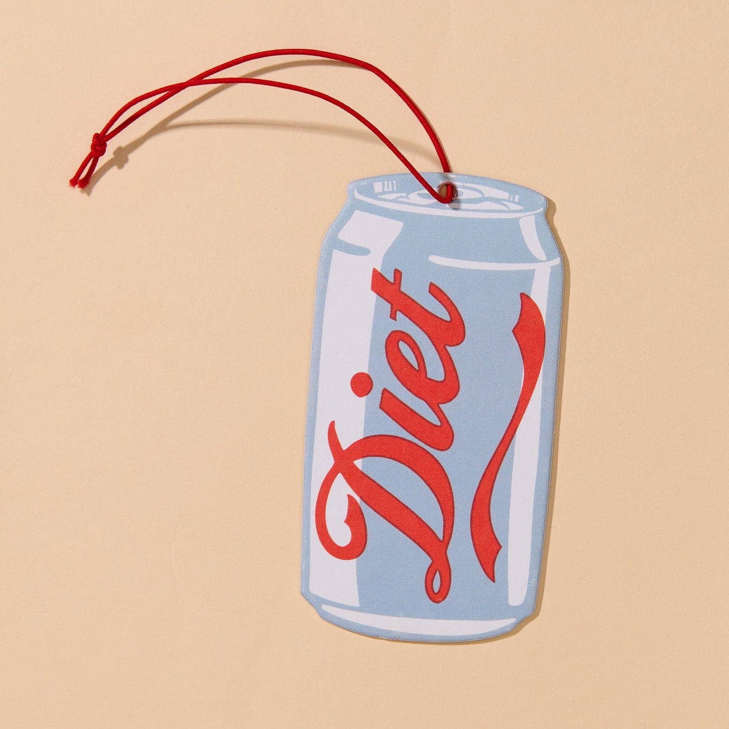 A novelty Diet soda can-shaped wall hanging or ornament with a red hanging string, shown on a solid beige background.