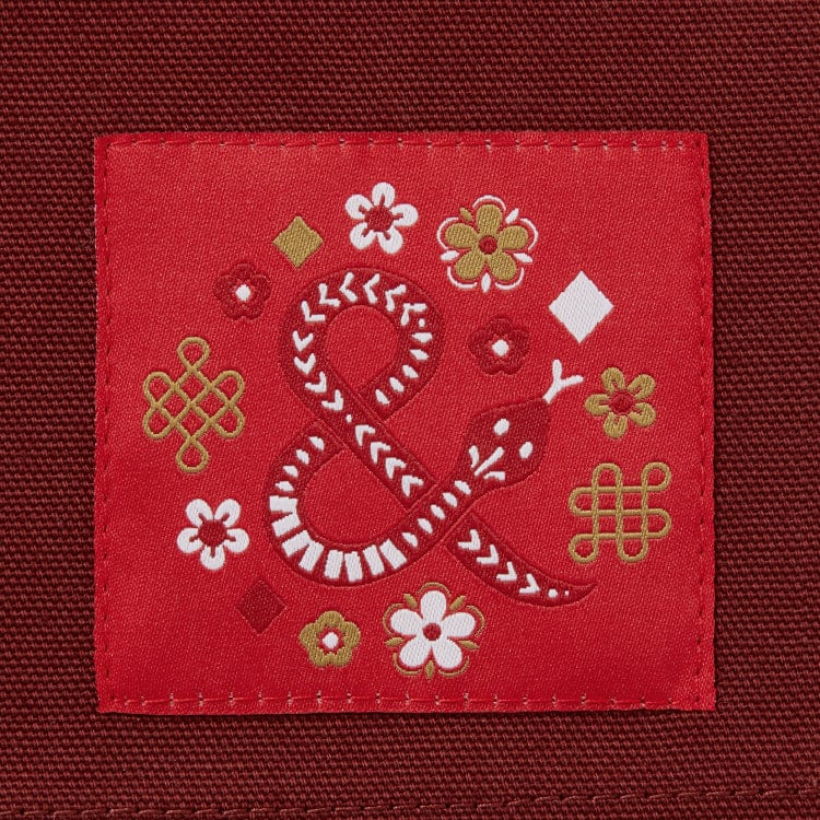 Cinnamon colored apron with mauve straps. This apron has a design that is dedicated to Dim Sum and has a steamer basket full of smiling dumplings and one dumpling being grabbed by chopsticks. This photo is the ampersand logo of Hedley and Bennet with an asian flair.