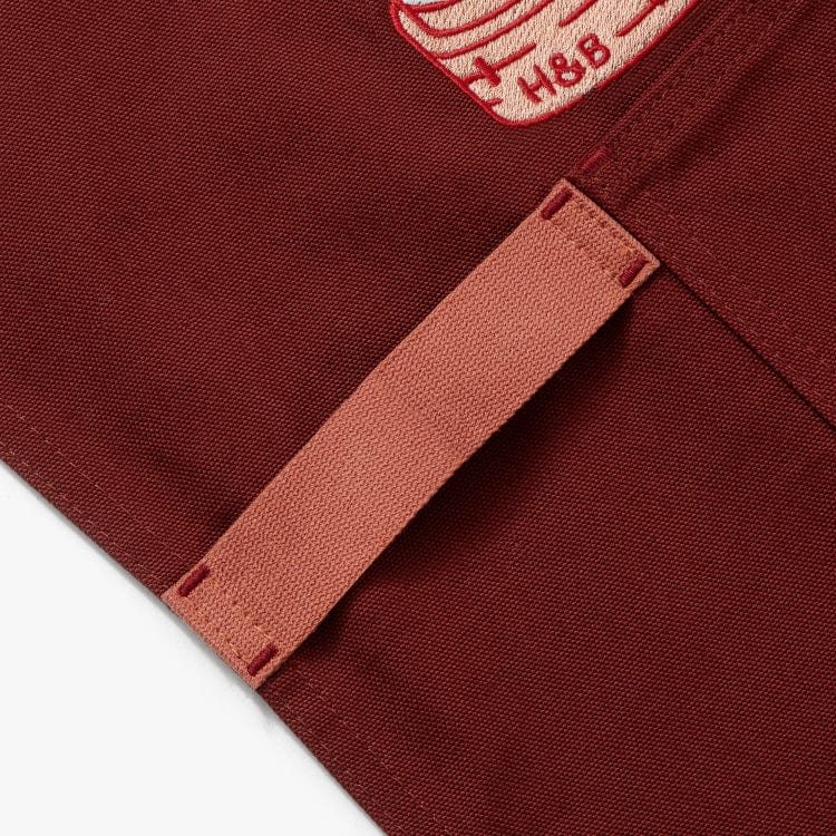 Cinnamon colored apron with mauve straps. This apron has a design that is dedicated to Dim Sum and has a steamer basket full of smiling dumplings and one dumpling being grabbed by chopsticks. This photo shows the detail of the towel loop.