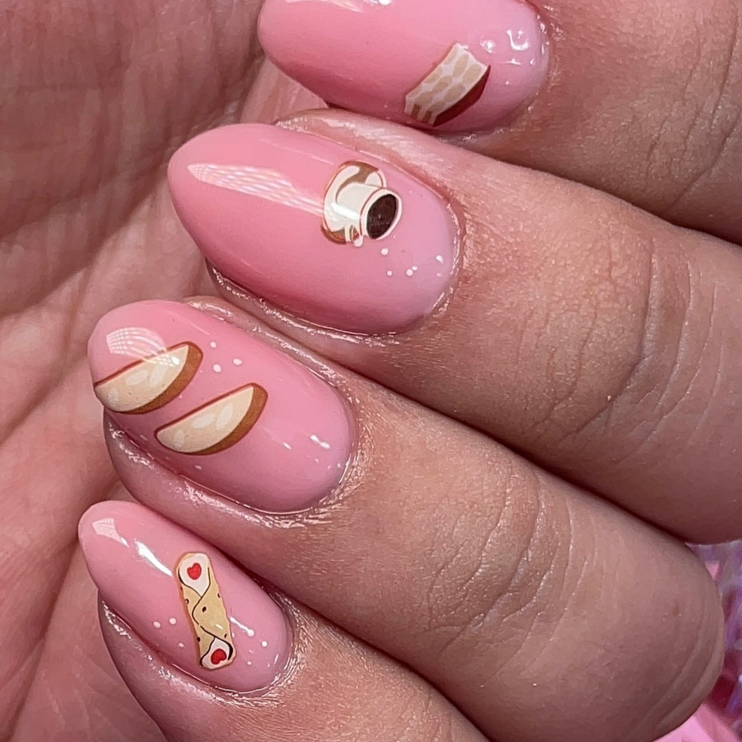 Set of decorative nail decals that look like Italian treats such rainbow cookies, pizzelles, espresso, panettone, and more. Shown on nails with pale pink nail polish.