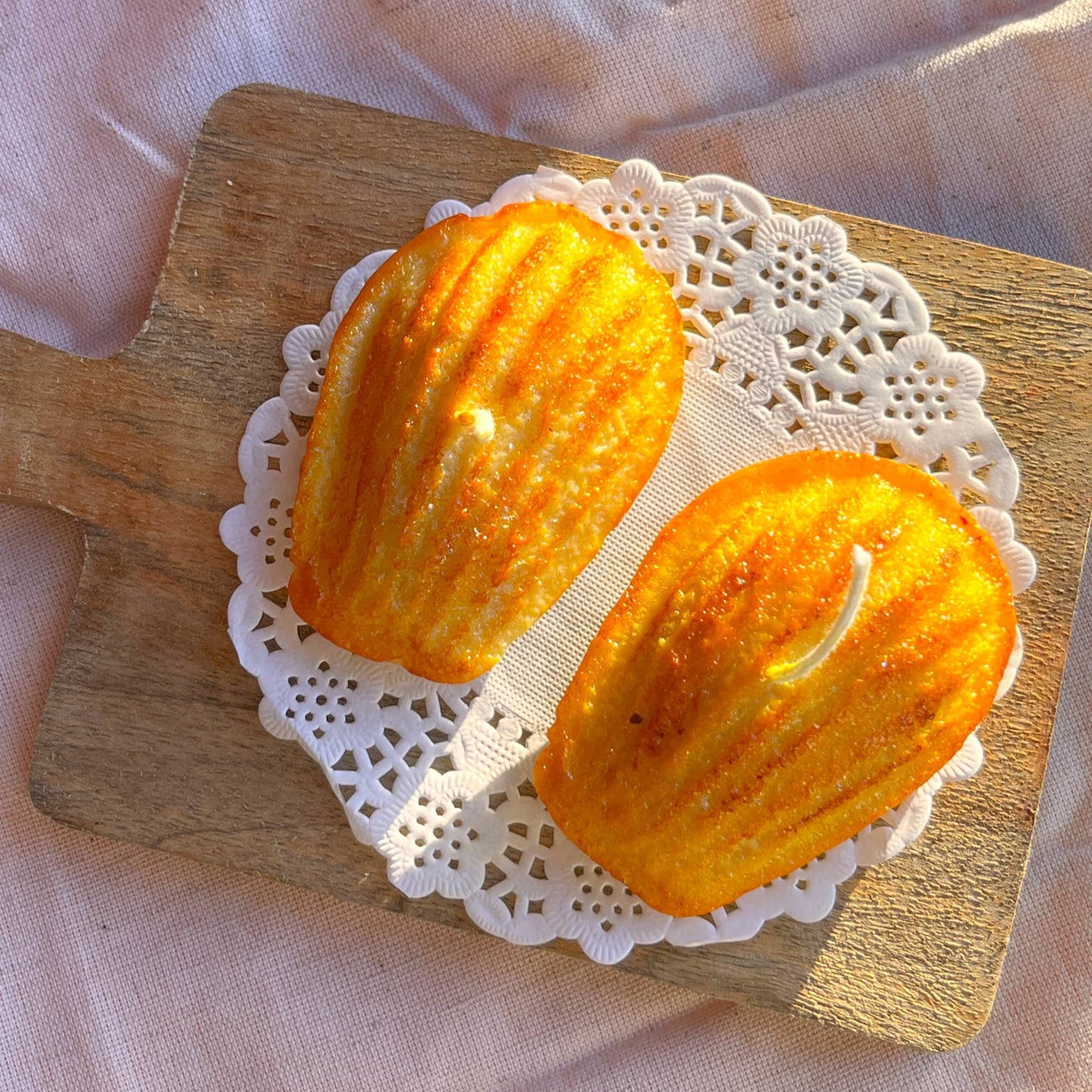 Set of two candles shaped like Madeleines (small French cakes) shown on a lace paper doily.