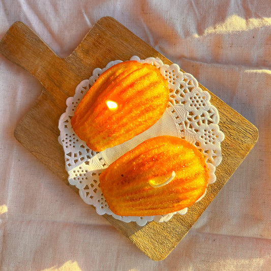 Set of two candles shaped like Madeleines (small French cakes) shown on a lace paper doily.