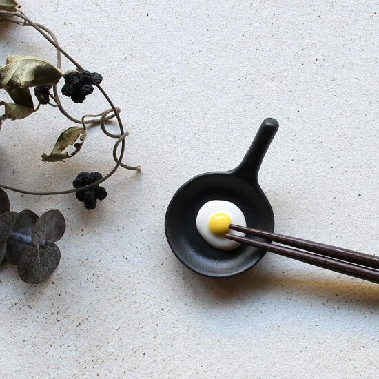 Mini cast iron fry pan with an egg on it. Chopstick holder