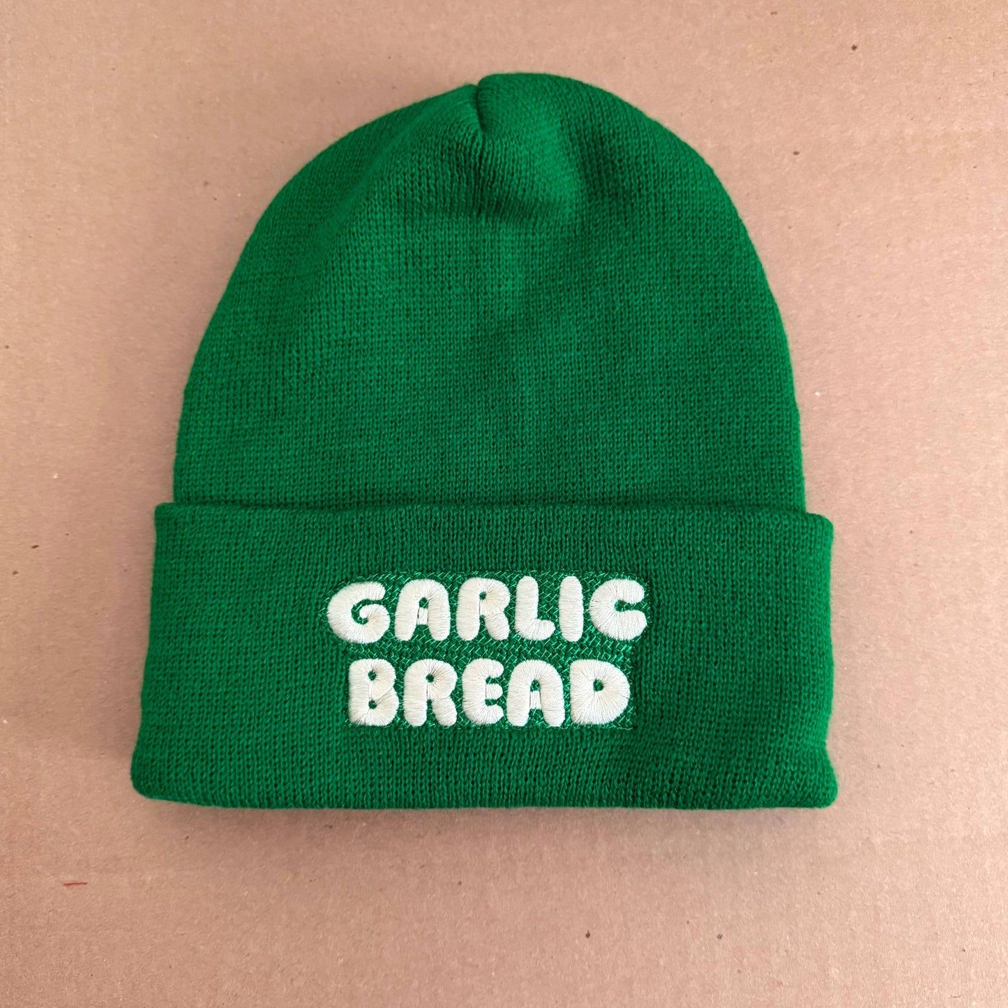 Green beanie with 'Garlic Bread' text on a beige background