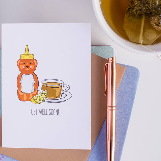 Honey bottle shaped like a bear, tea cup, and lemon wedge on a white background. Text "Get Well Soon!"