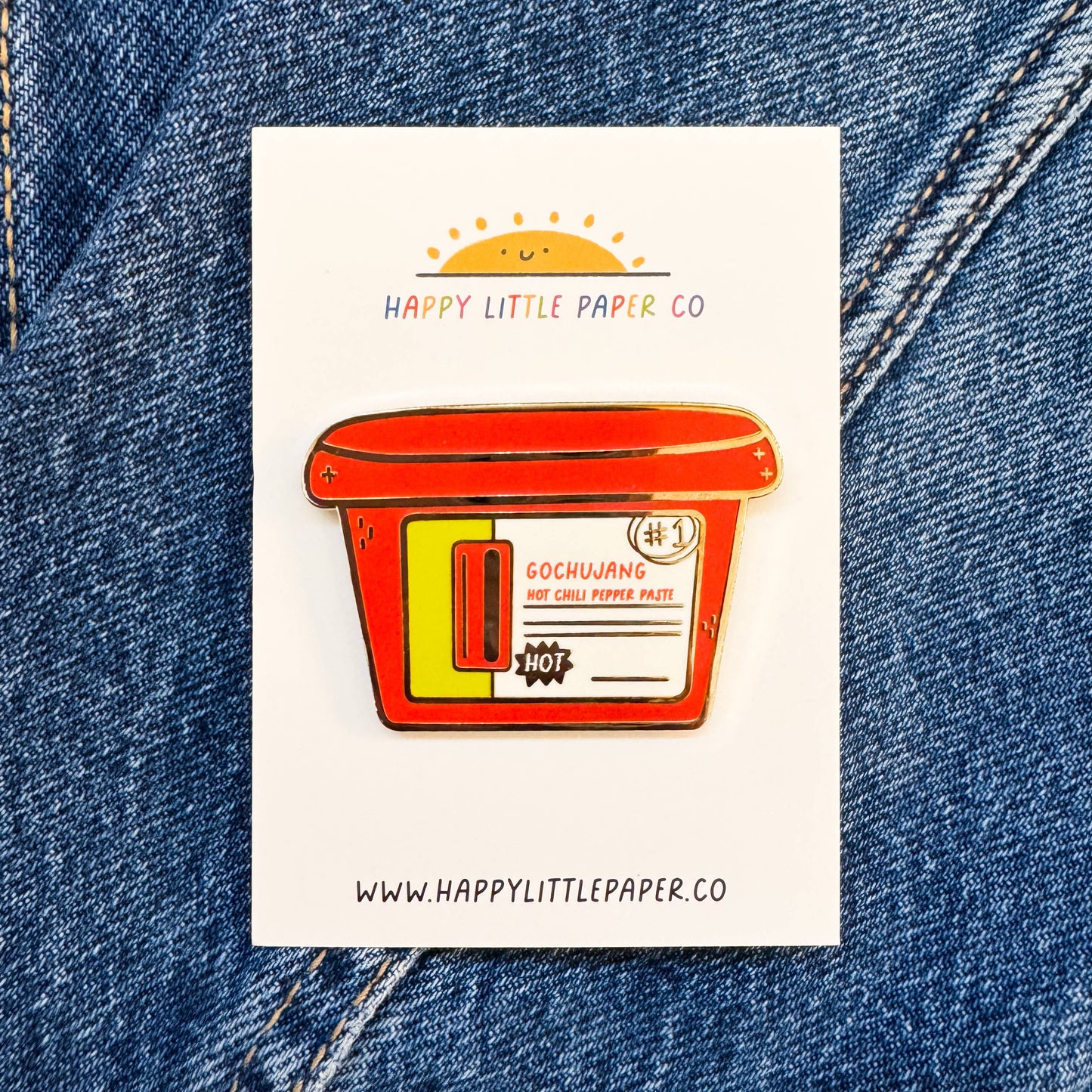 Sticker of a red container with yellow accents on a white background, placed on blue denim fabric.