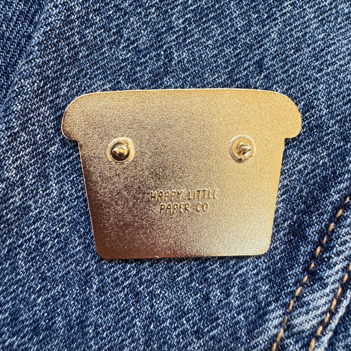 Brass label on a denim fabric with 'Happy Little Paper Co.' branding.