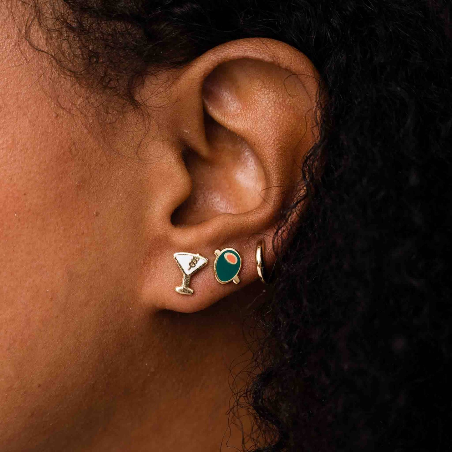 Showcasing earrings on ear lobe -- martini stud, olive stud and gold hoop