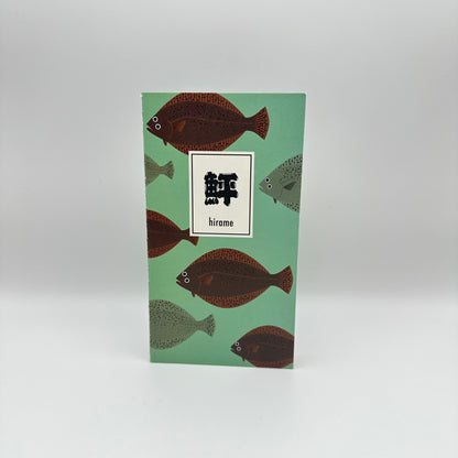 Teal notebook with brown and green flounder swimming on the cover. Japanese text box that reads Hirame.