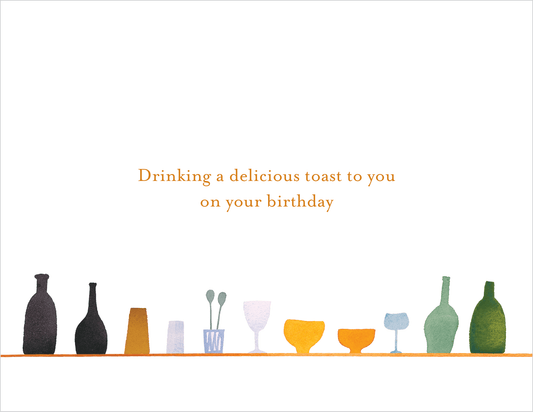 Decorative arrangement of bottles and glasses with a birthday message on a white background