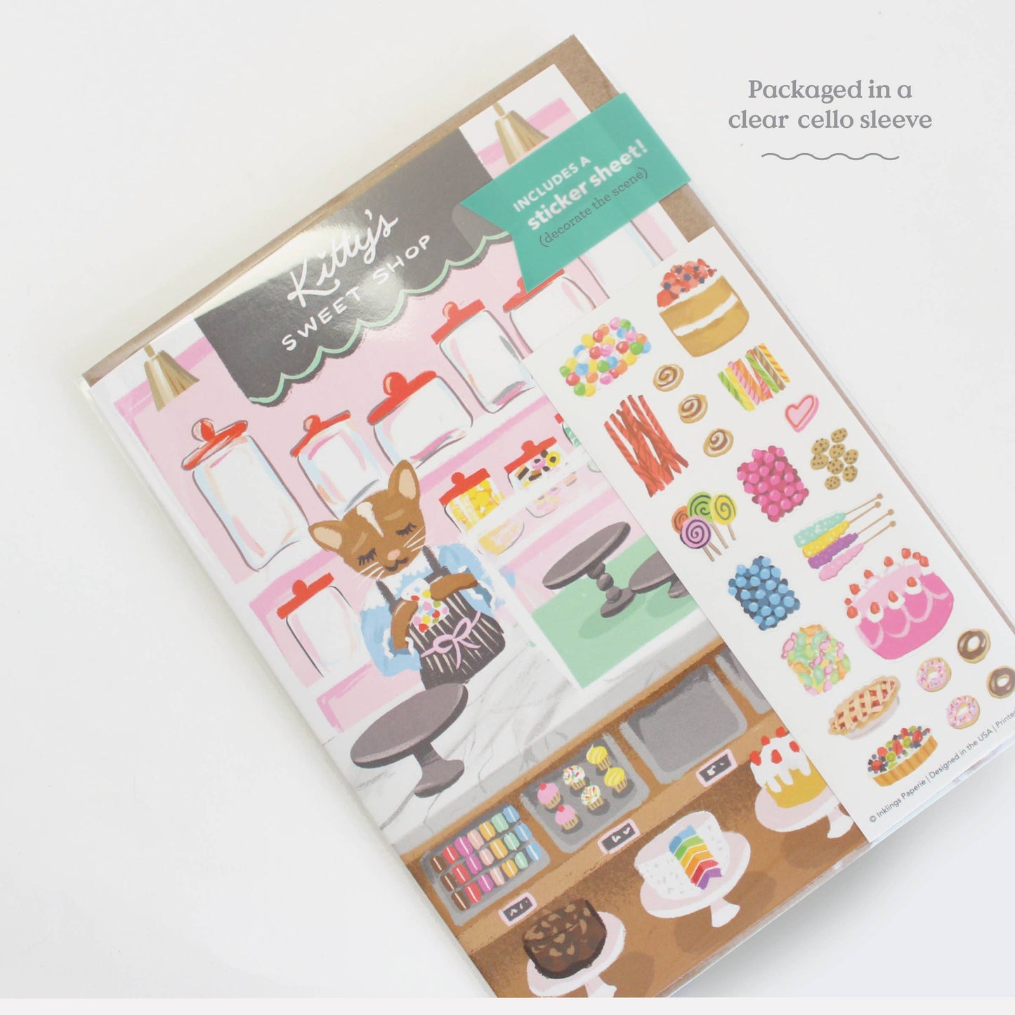 Interactive Card that includes stickers so one can decorate the front of the Sweet Shop with cakes and sweets. Text reads Kitty's Sweet Shop. Text that says: Packaged in a clear cello sleeve.