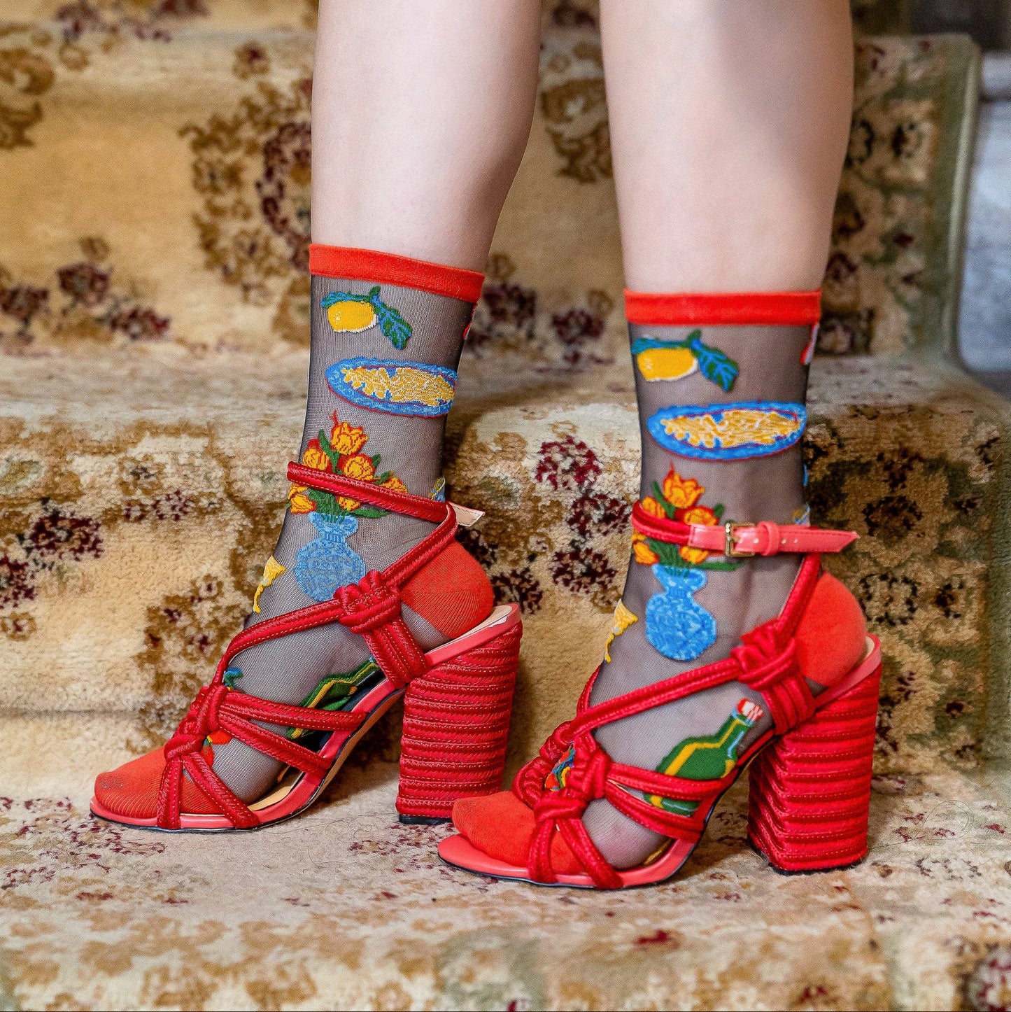 Red high-heeled shoes with colorful designs worn on patterned carpet