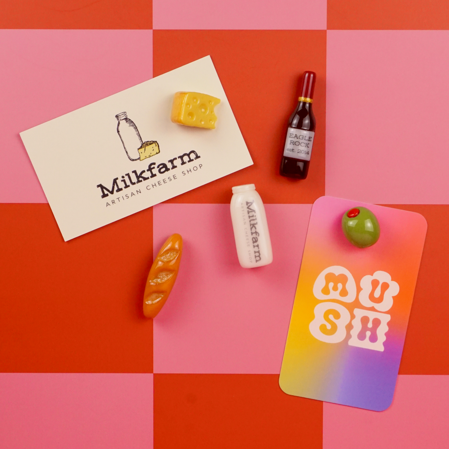 Small food item magnets and 2 business cards featuring Milkfarm and MUSH on a pink and red checkered background