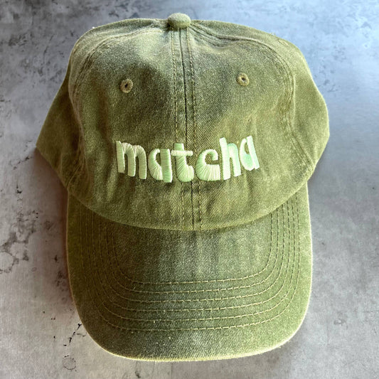 Faded olive green baseball hat with light green "matcha" embroidered in a retro font. Shown from different angles.