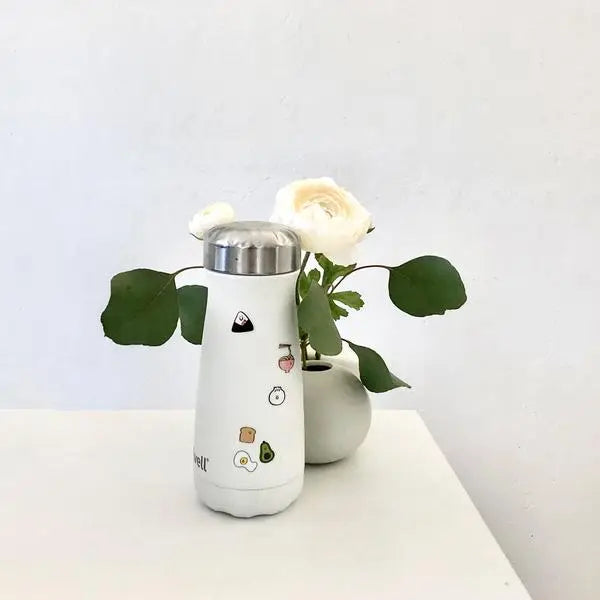 Waterbottle with mini stickers stuck to it. Little flower vase with white roses inside.