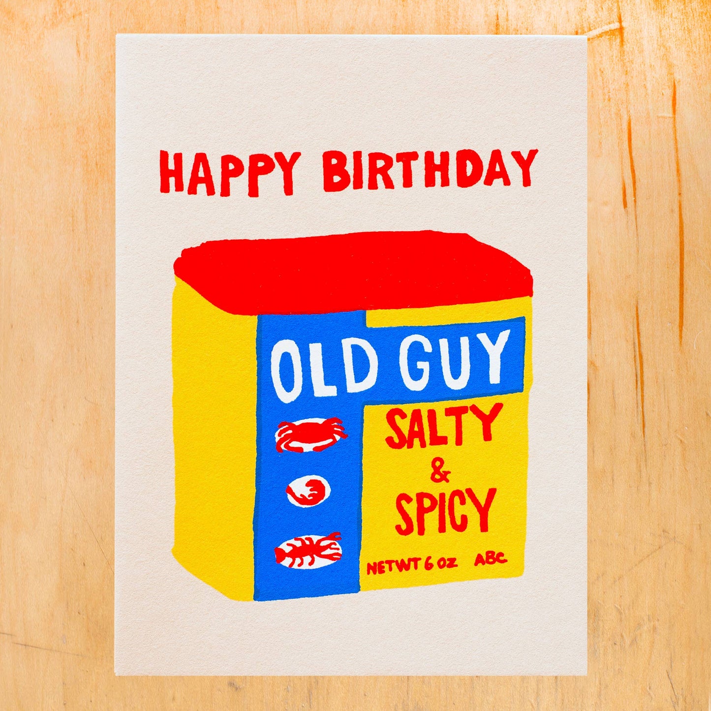 Birthday card with a box design labeled 'Old Guy Salty & Spicy' on a wooden surface.
