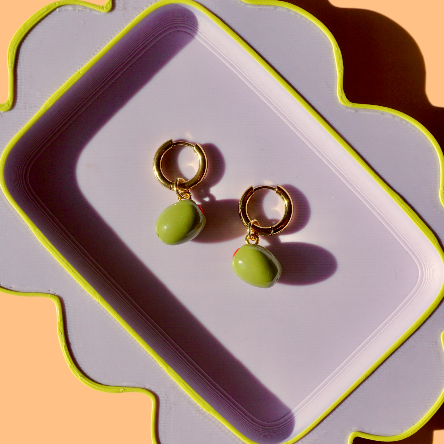 Gold hoop earrings with green olives on a decorative tray against an orange background