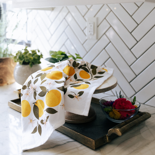 Kitchen scene with orange-themed towels on a wooden stand against a white tiled wall.