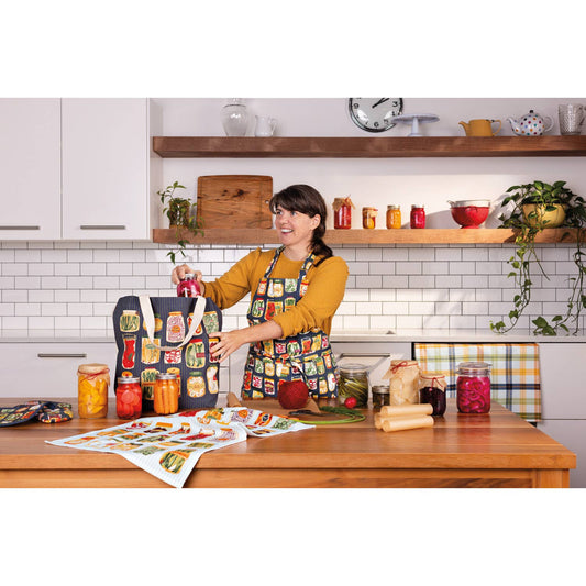 Woman in a kitchen holding a tote bag with a colorful design, surrounded by kitchen items.